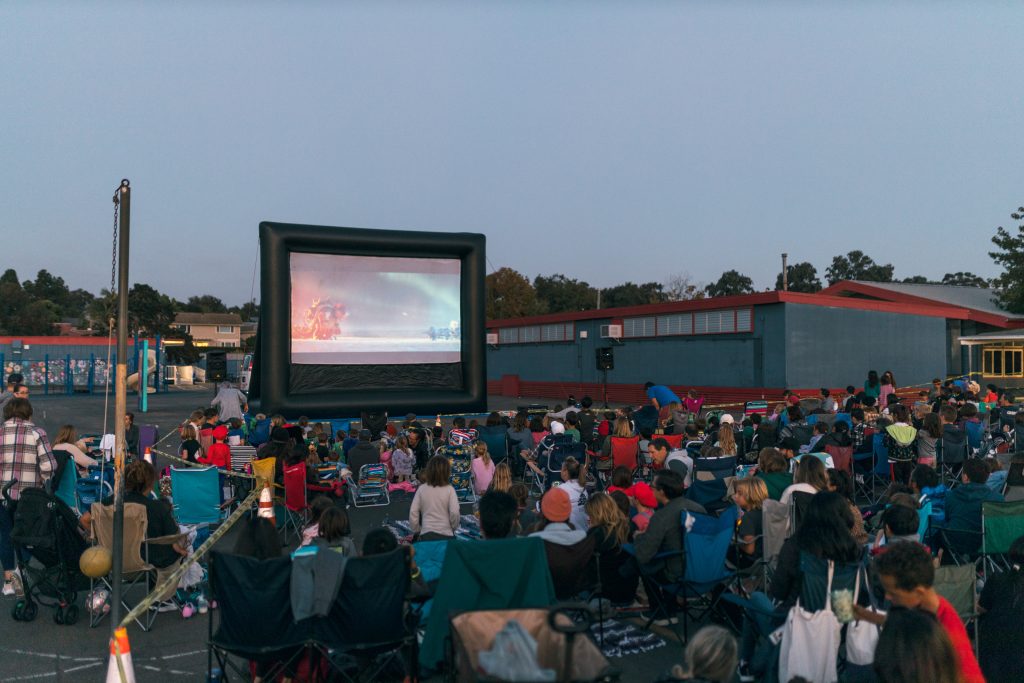 A large crowd watching Super Mario Bros on a FunFlicks® inflatable movie screen on the blacktop at Torrey Pines Elementary school.