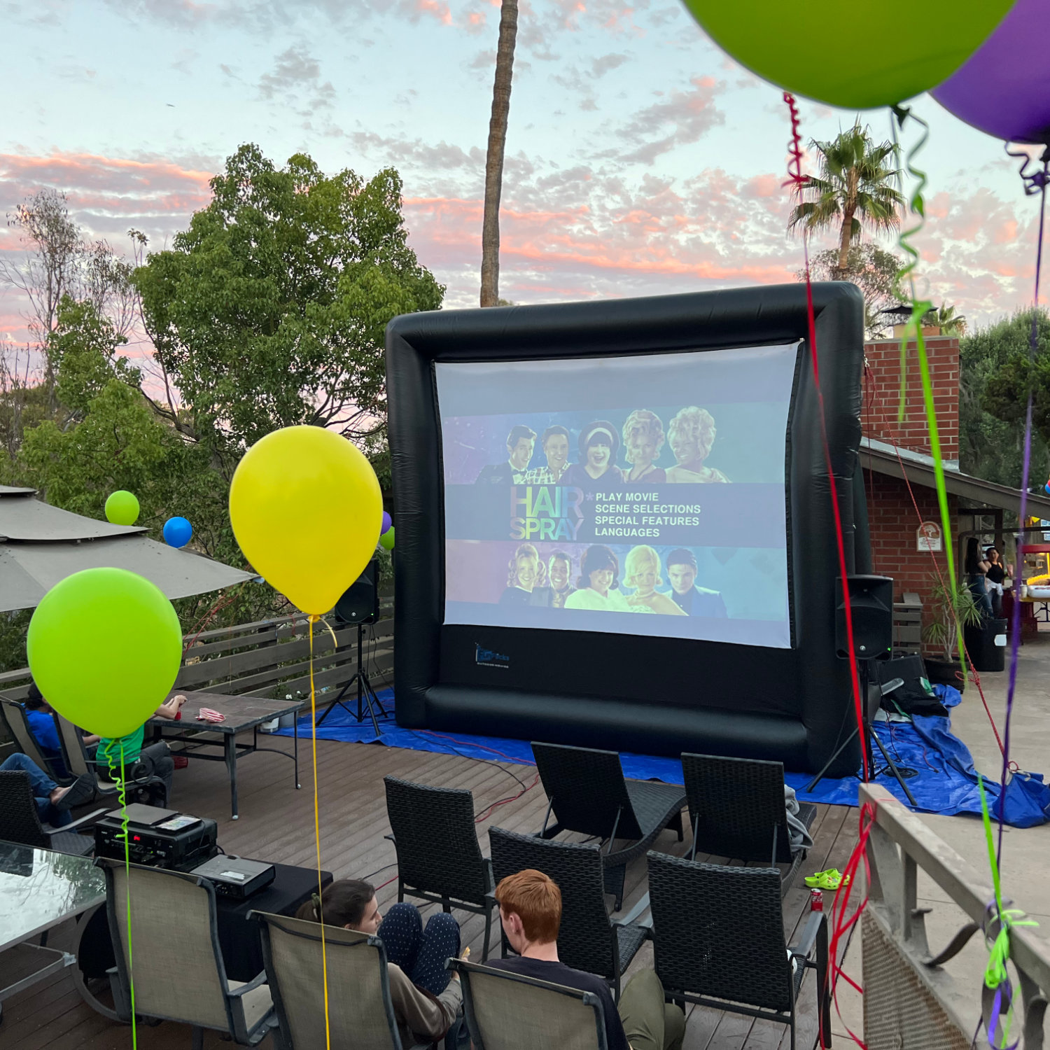 Friends and family watching a movie on a FunFlicks inflatable screen for a birthday party.