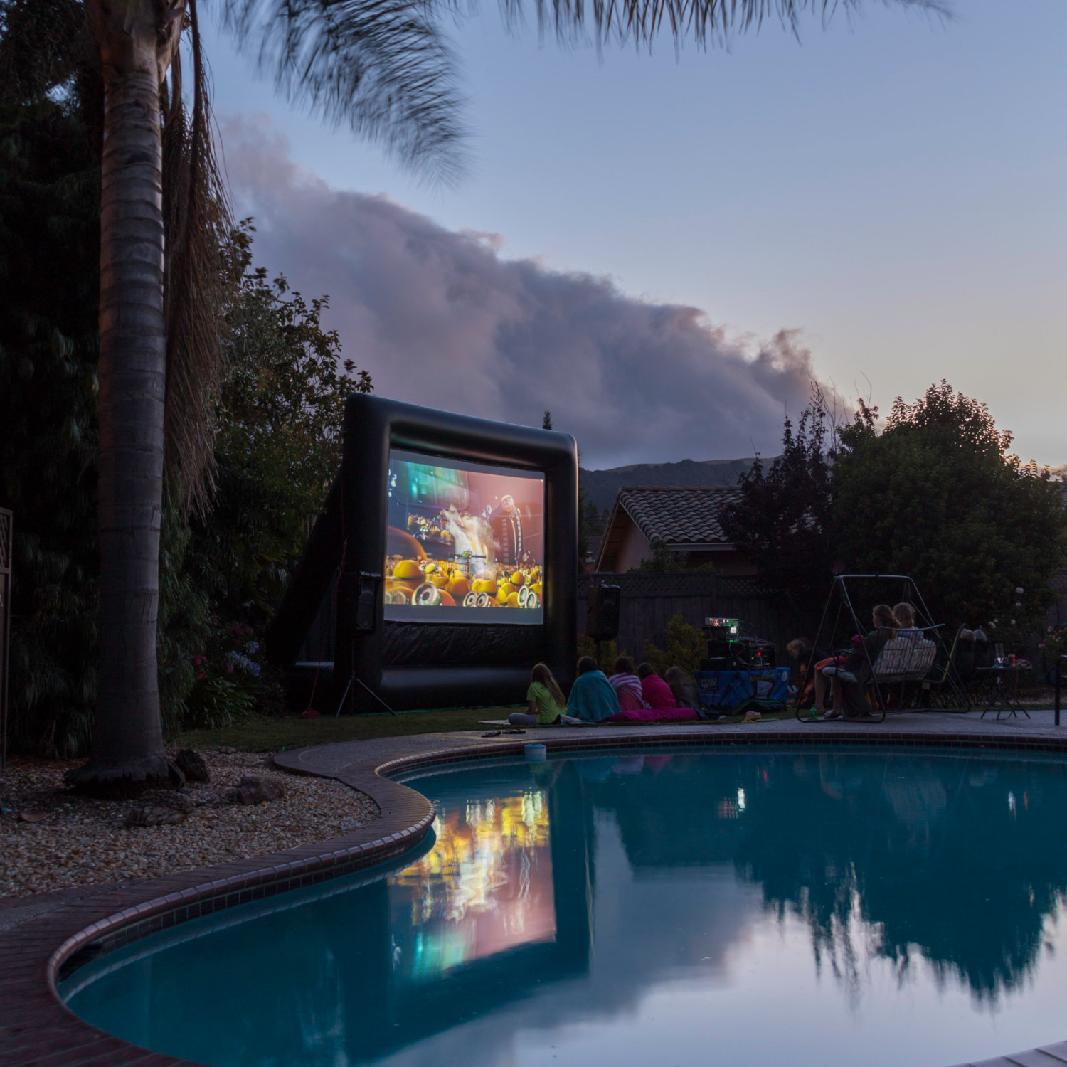 Kids watching a movie on a FunFlicks inflatable screen by the backyard pool.