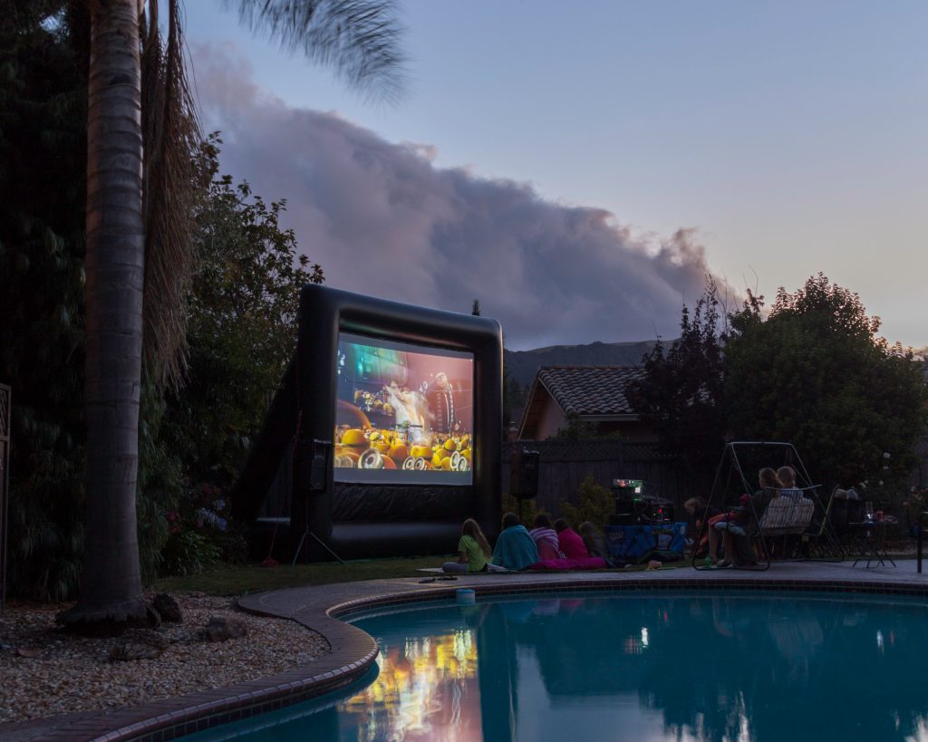 Family and friends watching a movie on a FunFlicks inflatable screen at their community pool.