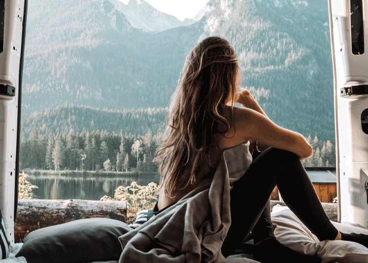 Woman staring at a lake view in the back of a van on a roadtrip